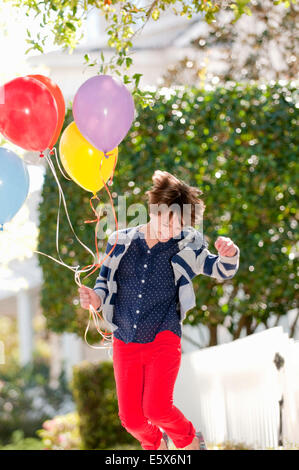 Ten year old girl jumping excitedly with bunch of balloons Stock Photo