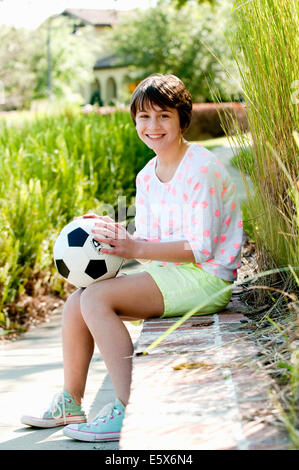 Portrait of ten year old girl sitting on park wall with soccer ball Stock Photo