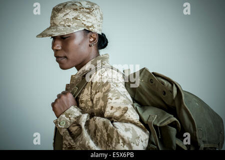 Side view studio portrait of female soldier with rucksack looking down Stock Photo