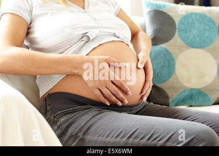 Pregnant woman sat relaxing on sofa Stock Photo