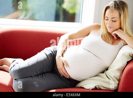 Pregnant woman sat relaxing on sofa Stock Photo