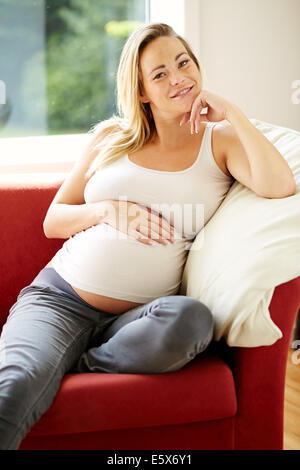 Pregnant woman sat relaxing on sofa Stock Photo