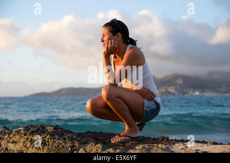 Mid adult woman crouching and gazing at caribbean sea from pier, Spice Island beach resort, Grenada, Stock Photo