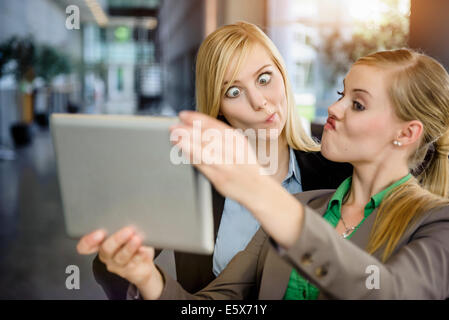 Two young businesswomen pulling faces and taking selfie on digital tablet in office Stock Photo