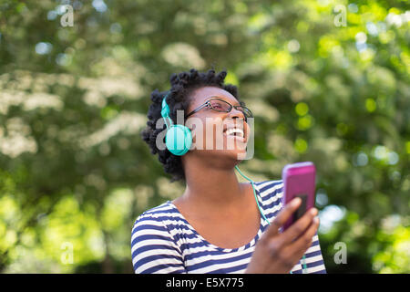Young woman in park listening and singing to music on headphones Stock Photo