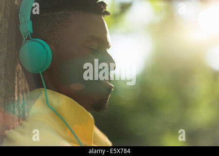 Close up of young man with eyes closed listening to headphones in park Stock Photo