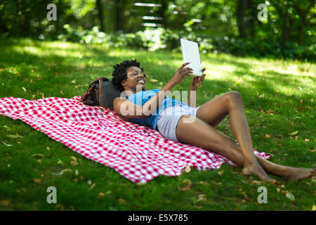 Young woman lying in park looking up at digital tablet Stock Photo