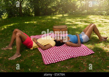 Young couple lying on picnic blanket in park on opposite sides Stock Photo