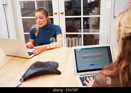 Two female colleagues using laptops in office Stock Photo