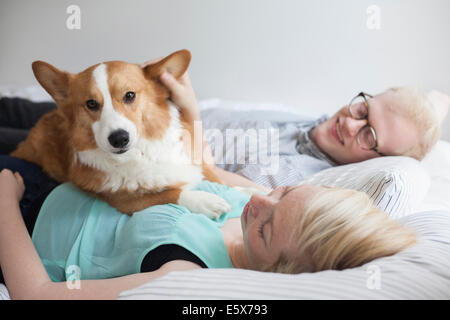Cute corgi dog lying on bed with young couple Stock Photo