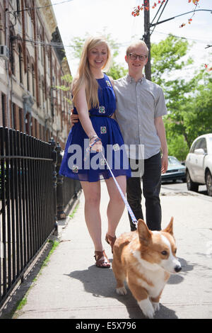 Young couple taking corgi dog for a walk along street Stock Photo