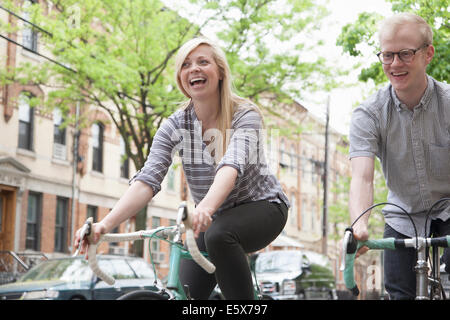 Young couple laughing whilst cycling along street Stock Photo