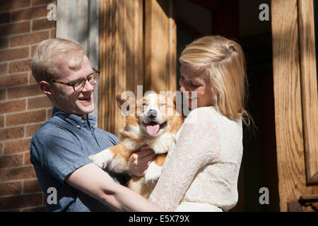 Happy young couple with corgi dog in arms outside front door Stock Photo