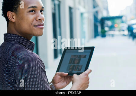 Young man on city street using digital tablet and looking over shoulder Stock Photo