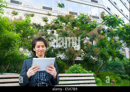 Mid adult businessman sitting on park bench looking at digital tablet Stock Photo