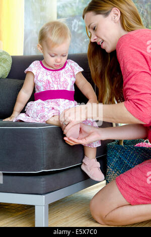 Mid adult mother putting on baby daughter's shoes Stock Photo