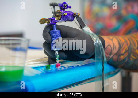 Close up of tattooist hand dipping tattoo gun's needle into red ink Stock Photo