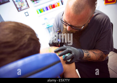 Mid adult man having shoulder tattooed in tattoo parlor Stock Photo