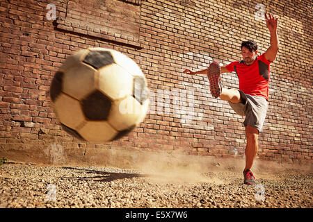 Young man kicking soccer ball on wasteland Stock Photo