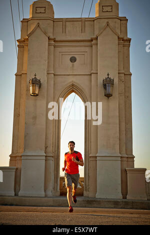 Young man running across city bridge Stock Photo