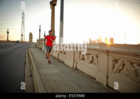 Young man running across city bridge at sunrise Stock Photo