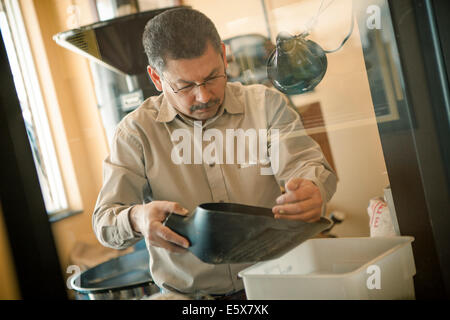Mature man using coffee bean scoop for coffee roasting machine in cafe Stock Photo