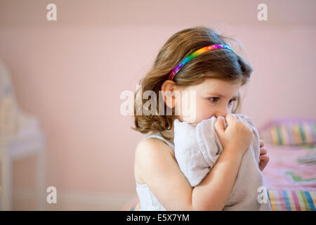 Unhappy three year old girl in bedroom holding comfort blanket to face Stock Photo