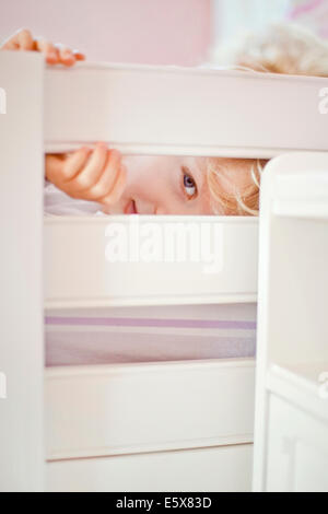 Close up portrait of four year old boy peeking through bed frame