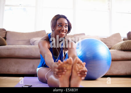 Young woman exercising and touching toes on sitting room floor Stock Photo