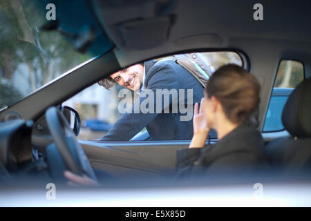 Young businesswoman driving and waving at male cyclist Stock Photo