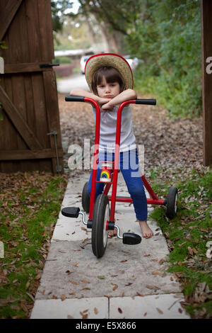 Portrait of four year old girl sitting on her tricycle in garden Stock Photo