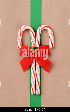 Two candy canes on a plain brown paper wrapped present with a green ribbon and red bow. High angle shot filling the frame in ver Stock Photo