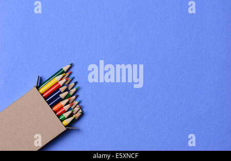 High angle shot of a box of multi-colored pencils on a blue background. The pencils are part way out of the box which is at an a Stock Photo