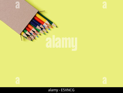 High angle shot of a box of multi-colored pencils on a yellow background. The pencils are part way out of the box which is at an Stock Photo