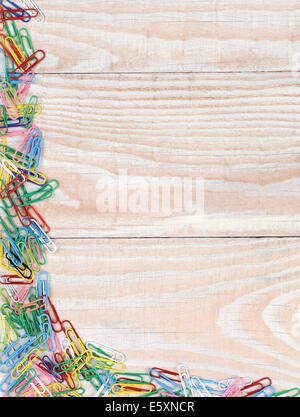 Paper clips in random pattern on two sides of the image. A whitewashed wood background with multi colored paper clips. Stock Photo