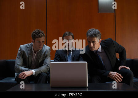 Business associates sitting side by side on sofa looking at laptop computer in disbelief Stock Photo