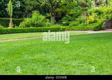 Green fresh lawn and brick pathway in a large public garden with hedges and flower beds Stock Photo