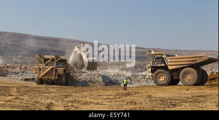 A supervisor directs Hitatchi haul trucks being loaded with ore by a massive Liebherr excavator in an open cast copper mine. Stock Photo