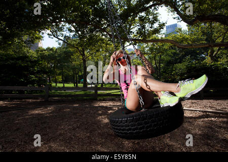 Young Blond Athletic woman sitting and rocking on a tire swing in Central Park Stock Photo