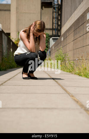 Stressed/tearful young woman,crouching down with her head in her hands. Stock Photo