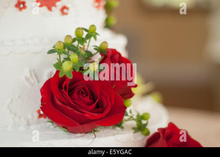 Red roses and greenery decorate a simple buttercream wedding cake Stock Photo
