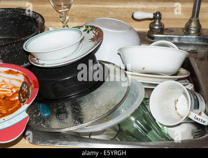 A stack of dirty dishes in the sink that need washing. Stock Photo