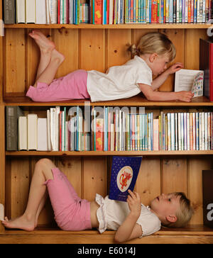 Young girls reading books whilst lying in a bookcase Stock Photo