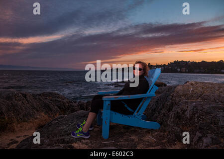 Portrait of young  woman sitting in Blue Adirondack chair-McNeil bay, Victoria, British Columbia, Canada. Stock Photo