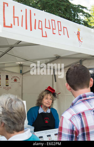 West Dean, Chichester, UK. 9th August, 2014. The Chilliqueen complete with chilli red hat serves customers at her stall at the Chilli Fiesta at West Dean, August 2014. UK weather.  Credit:  MeonStock/Alamy Live News Stock Photo