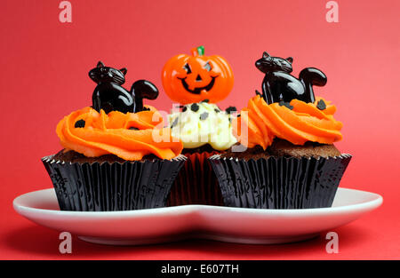 Happy Halloween orange and black decorated cupcakes with black cats and jack-o-lanterns on white heart plate. Stock Photo