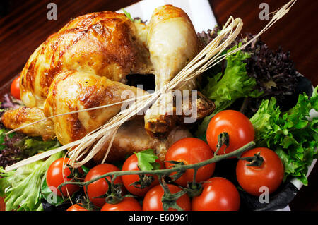 Platter of delicious roast chicken turkey with salad greens and red tomatoes on the vine. Stock Photo