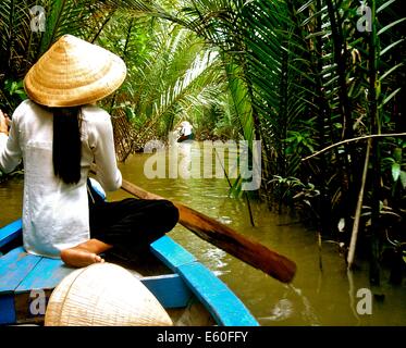 A Vietnamese lady wearing a traditional conical hat, sits on her wooden boat in the Mekong Delta, near Ho Chi Minh city, Vietnam Stock Photo