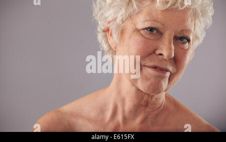 Close-up portrait of old caucasian female face against grey background. Senior woman with wrinkled skin looking at camera. Stock Photo