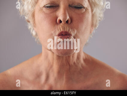 Cropped portrait of senior woman puckering lips. Mature female grimacing against grey background Stock Photo